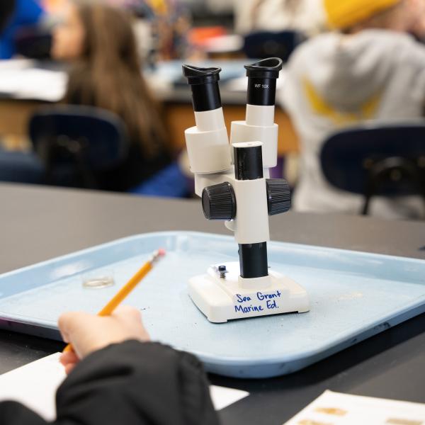 A microscope sits on a table in a classroom.