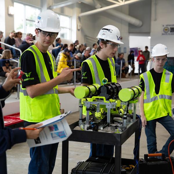 Several students in neon safety vests and hard hats stand around an ROV.